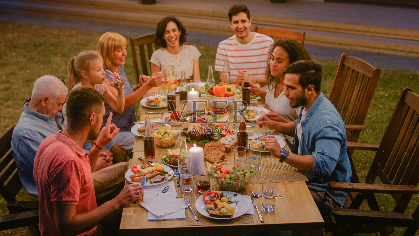 一群朋友围坐在桌旁亲戚朋友，年轻人和老年人在吃，喝，传递菜，开玩笑和玩。游园会晚会庆祝活动。照片摄影图片