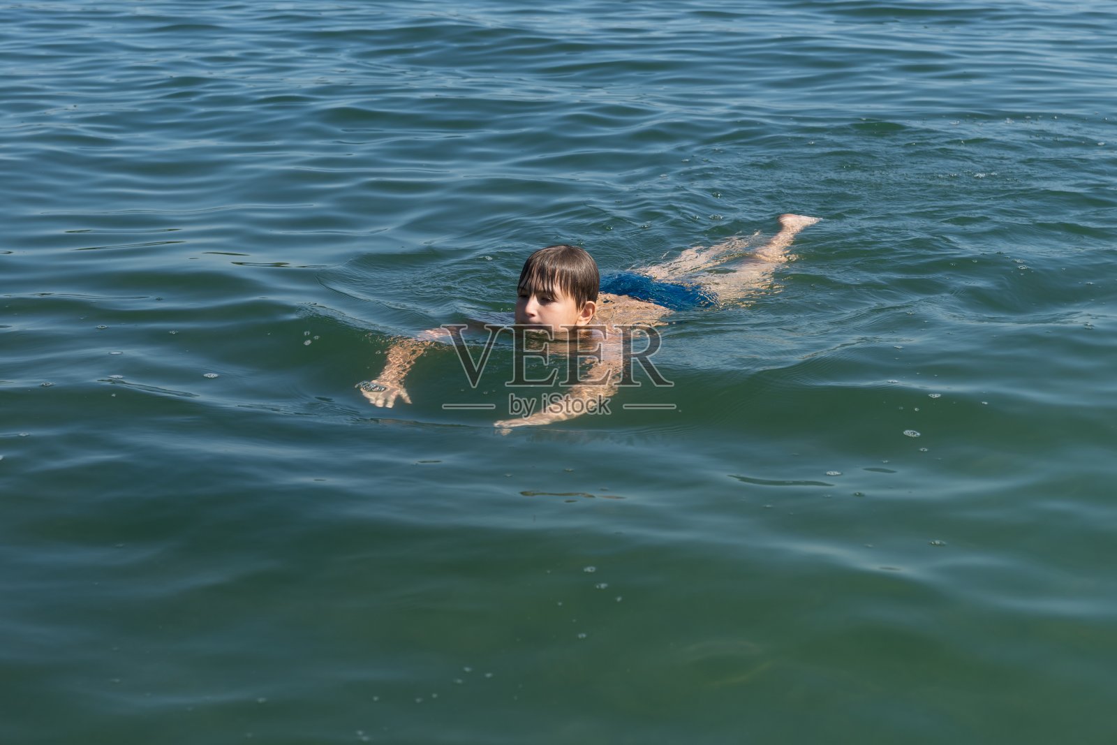 一个11岁的男孩正在蓝色的水中游泳。照片摄影图片