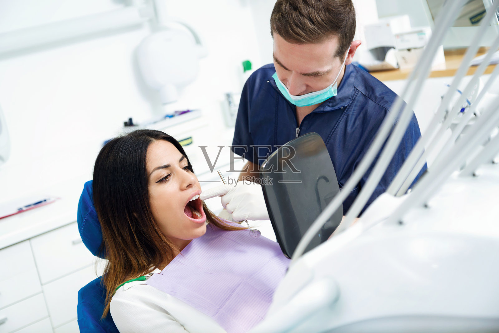 在牙科诊所的镜子前，年轻貌美的牙医和满意的病人看着美白治疗的结果。照片摄影图片