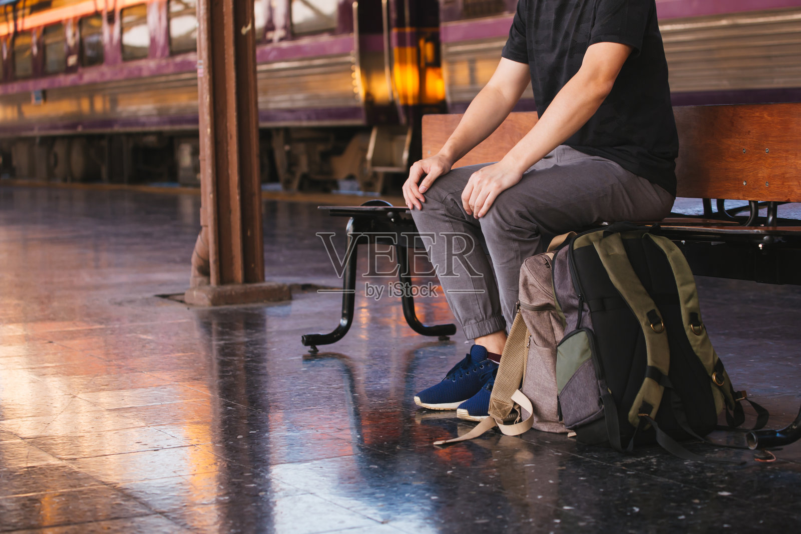 年轻的亚洲男性旅行背包客坐在和等待在曼谷的铁路站台，泰国-亚洲旅游的概念照片摄影图片