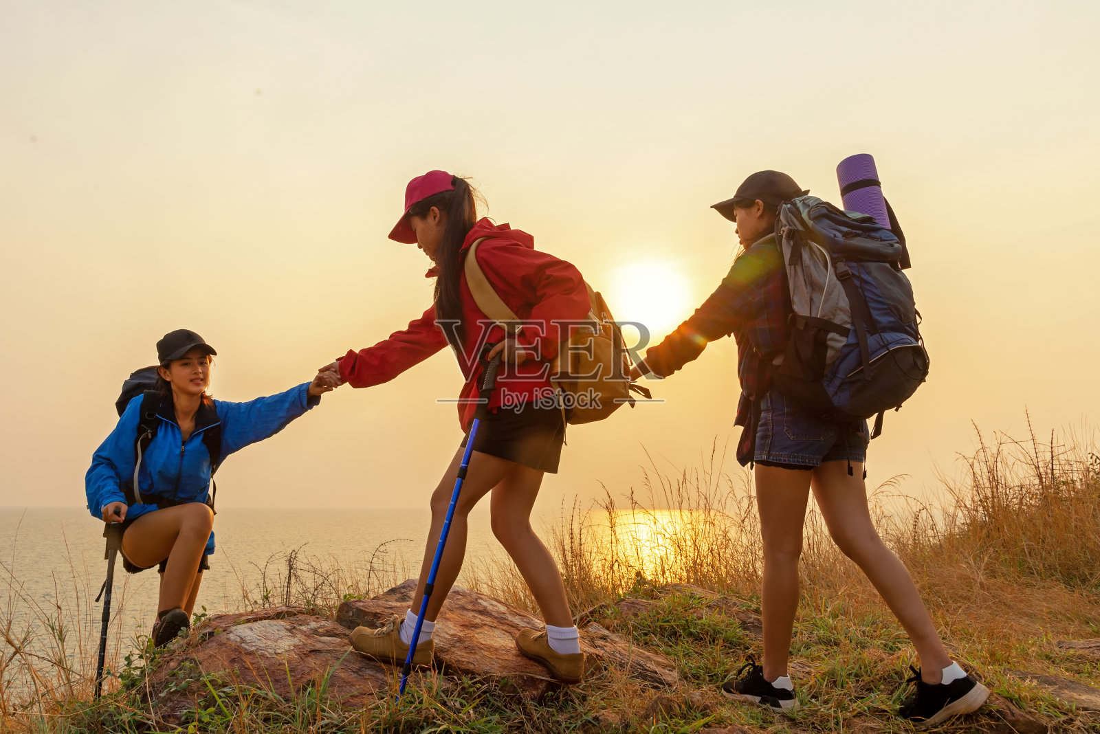 团队徒步女团队帮助她的朋友爬上日落山的最后一段。旅行团队和家庭放松散步在户外生活方式的冒险和露营。旅游夏季生活理念。照片摄影图片