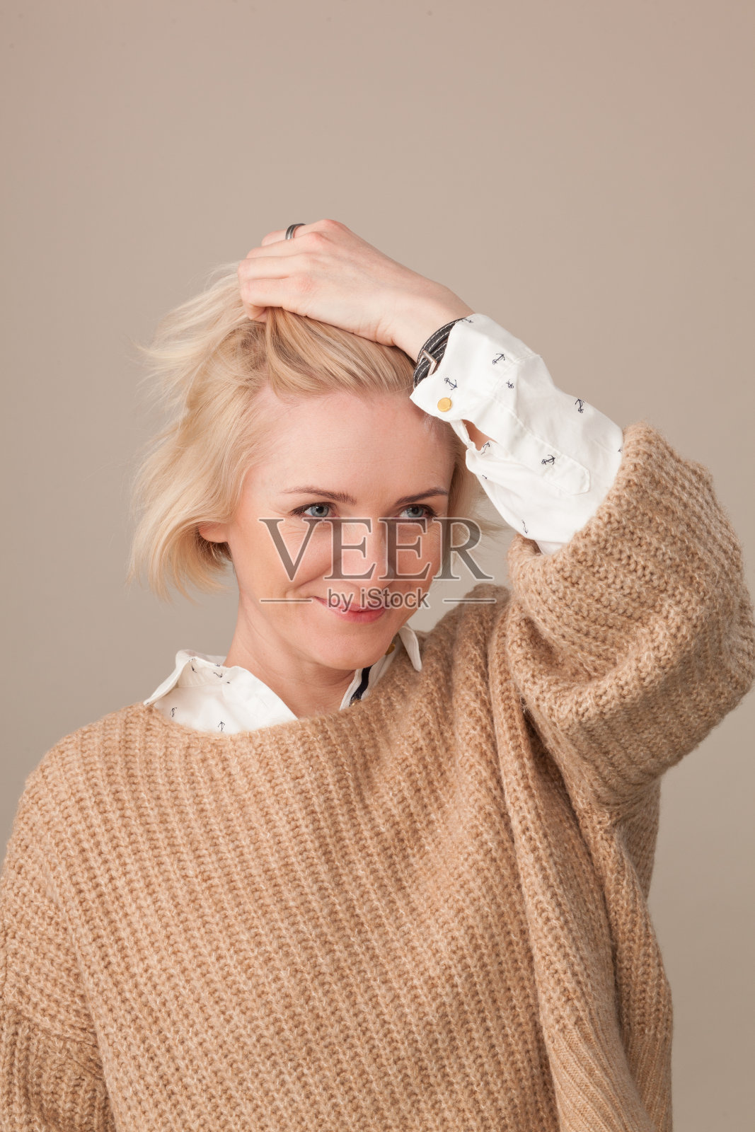 一个迷人的40岁金发女人在米色的背景米色毛衣的工作室肖像照片摄影图片