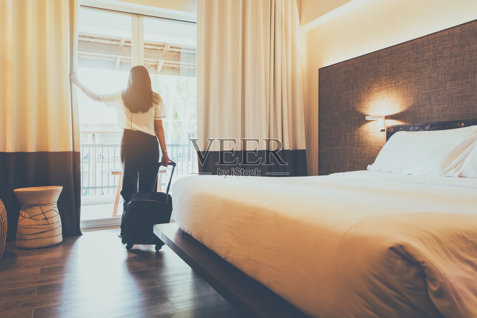 亚洲女性住在酒店房间里。打开房间里的窗帘，带着行李。人的概念是舒适的旅行。照片摄影图片