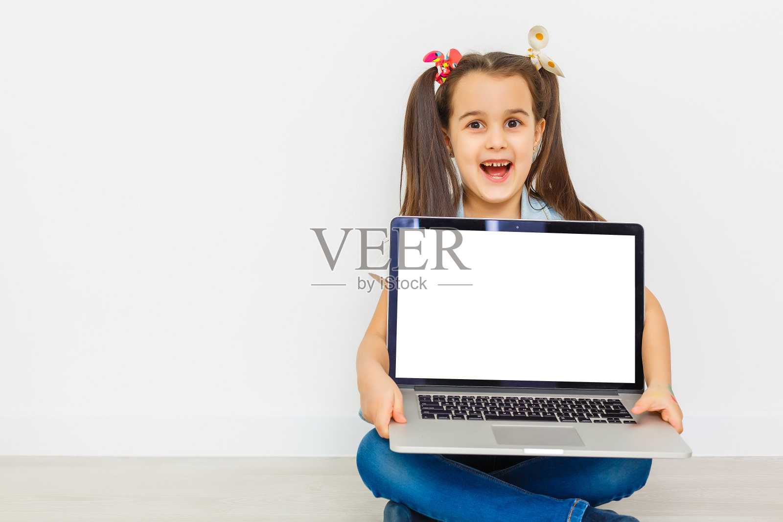 可爱的小女孩坐在地板上，带着她的笔记本电脑，戴着眼镜，孤立的白色照片摄影图片