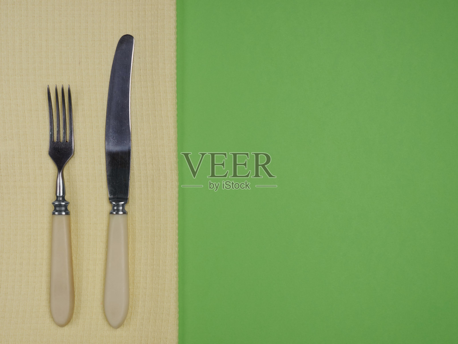 不锈钢叉和刀与象牙处理在黄色毛巾在绿色背景与copyspace照片摄影图片