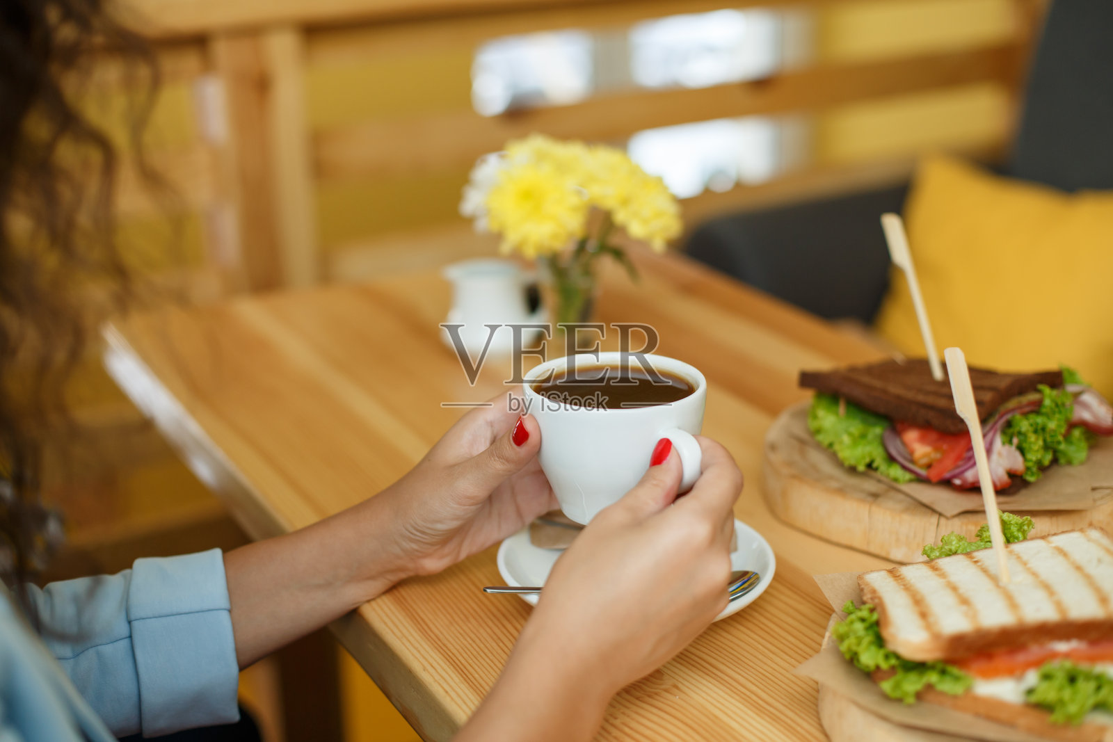 一个女人拿着一杯咖啡，后面的木桌上放着一个三明治。照片摄影图片