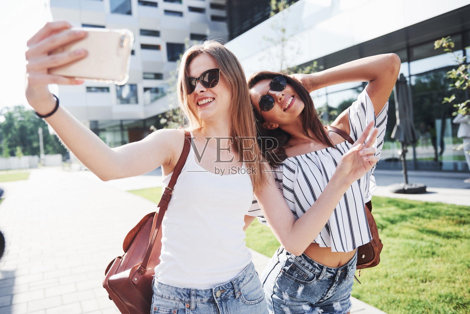 两个漂亮的女孩背着背包一起走在城市里。漂亮可爱的朋友分享秘密照片摄影图片