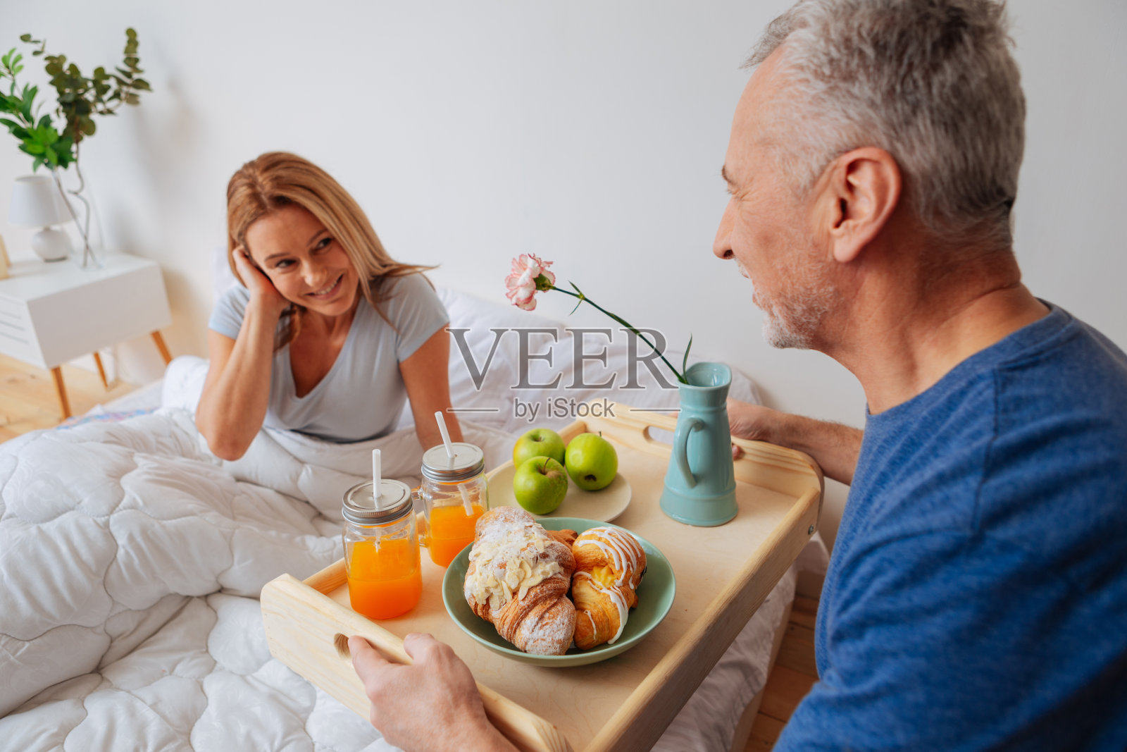 妻子看着拿着早餐和鲜花托盘的丈夫照片摄影图片