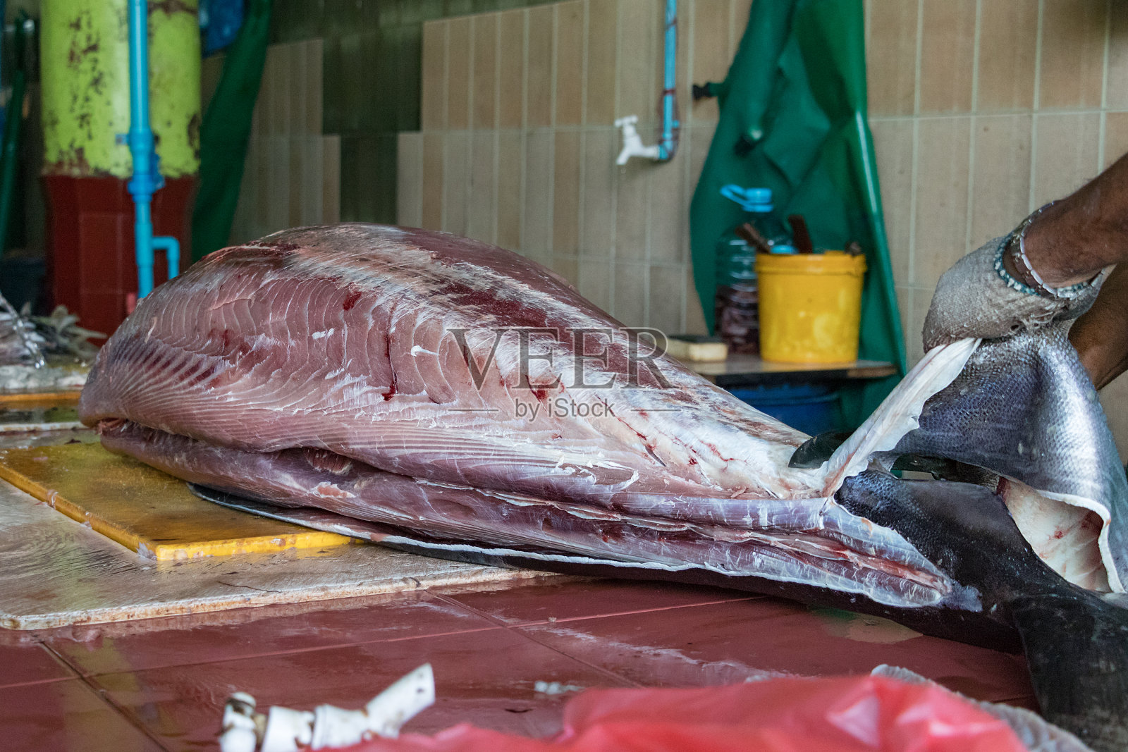 在马尔代夫马累的鱼市，一名男工人正在切一条大金枪鱼照片摄影图片