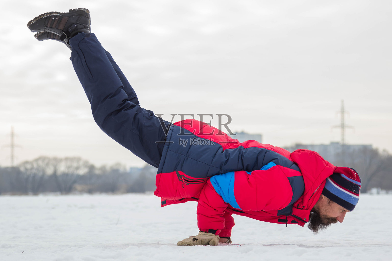 一个中年男子正在一条冰冻的河上做瑜伽。Mayurasana(孔雀的姿势)照片摄影图片