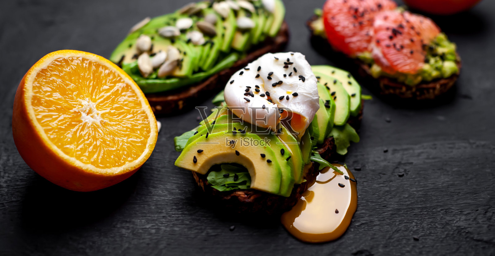 健康的早餐吐司，上面有鳄梨、芝麻、葡萄柚、橙子和鸡蛋，背景是混凝土照片摄影图片