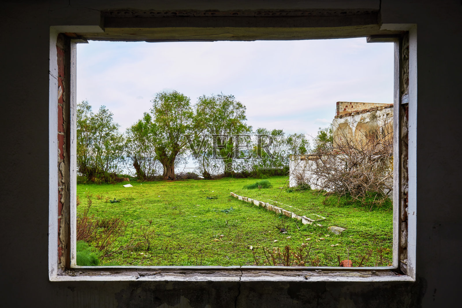 一个破旧的房子的内部，一个破碎的窗框，观看绿色的草地田野景观照片摄影图片
