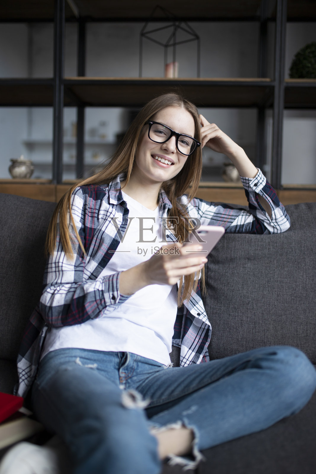 一个可爱的女孩戴着眼镜和手机在沙发上的肖像照片摄影图片