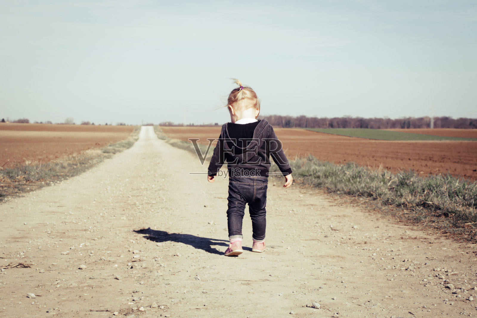 小女孩走在一条尘土飞扬的乡村道路上的背影照片摄影图片