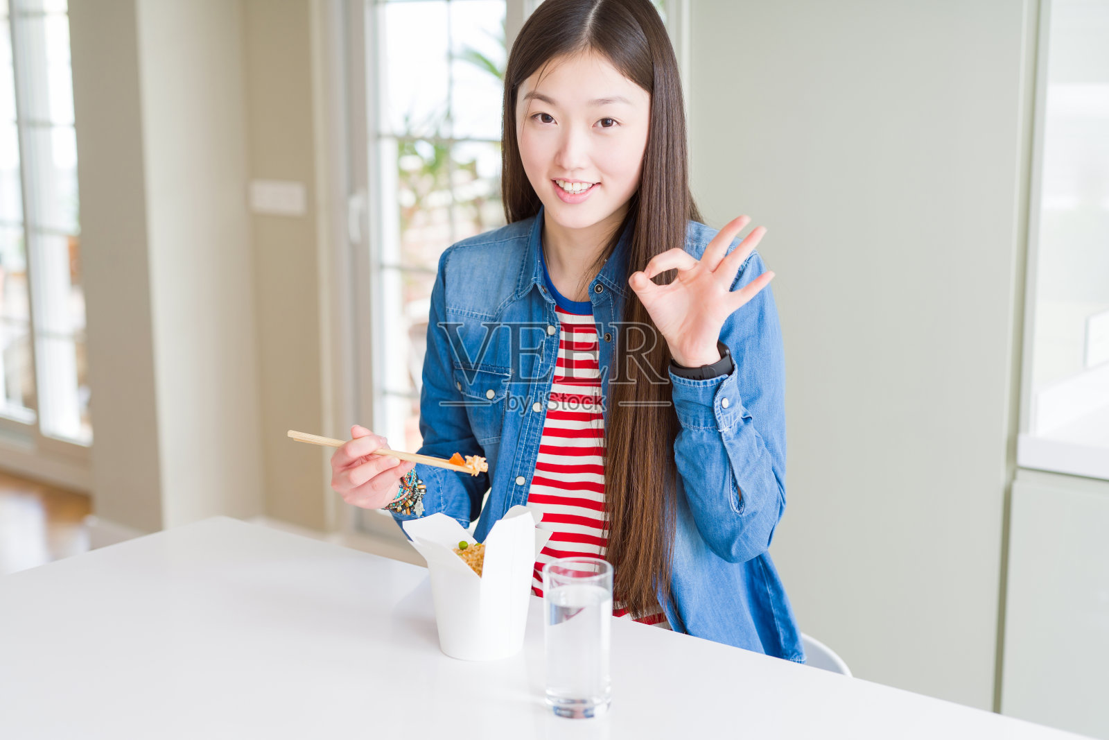 美丽的亚洲女人吃亚洲大米在外卖盒做ok手势与手指，优秀的象征照片摄影图片