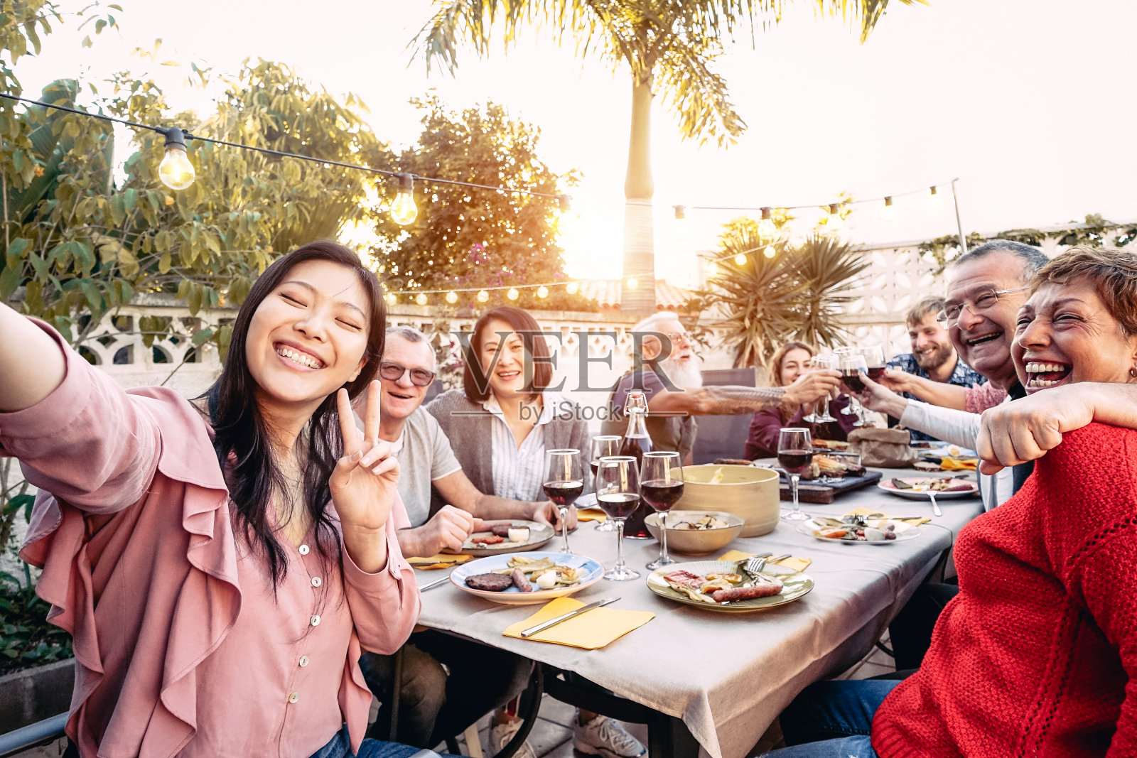 快乐的家庭在户外晚餐时用红酒举杯庆祝-不同年龄和种族的人在烧烤派对上享受乐趣-食物和饮料，退休和年轻人的概念照片摄影图片