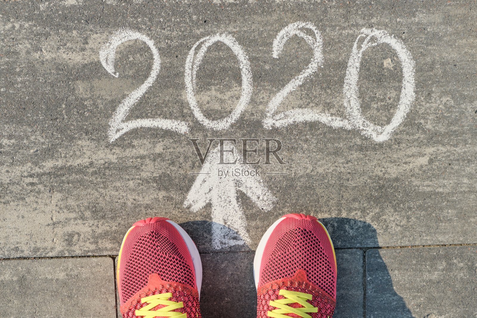 2020箭头向前，写在灰色的人行道上穿着运动鞋的女人腿，俯视图照片摄影图片