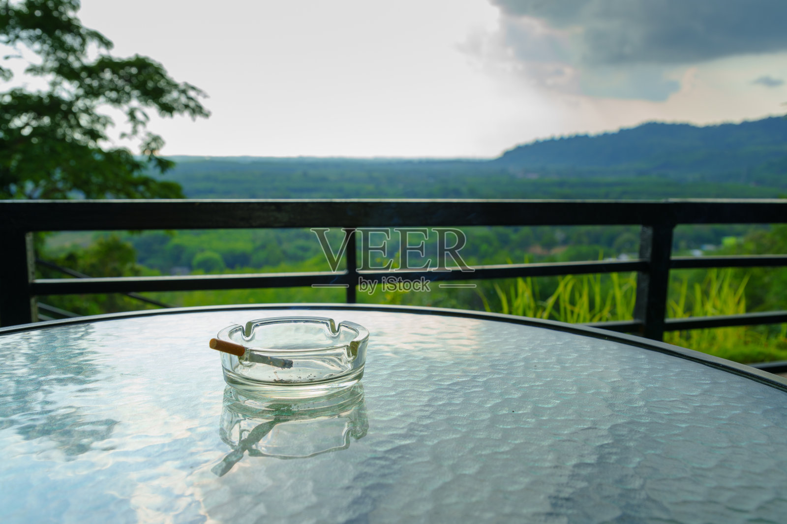 在玻璃桌子上的烟灰缸里抽烟。阳台上以树木、森林和自然为背景。照片摄影图片