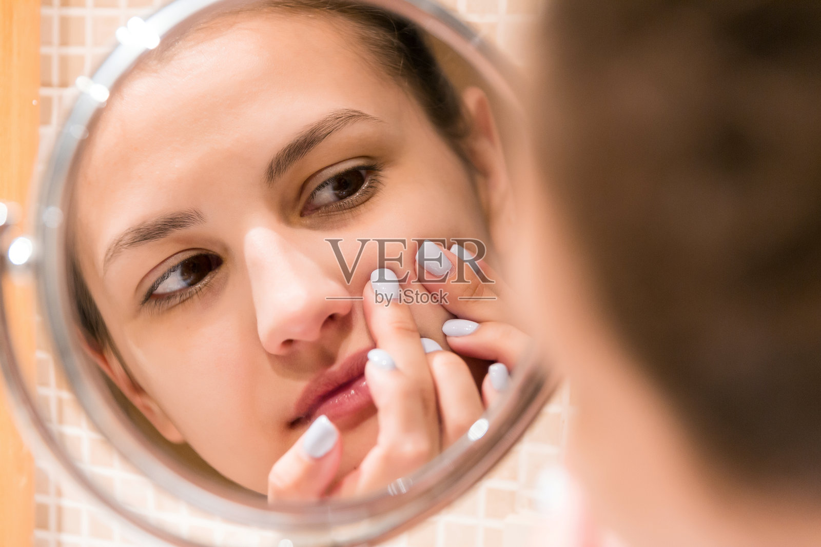 一个年轻的女孩在浴室的镜子前挤青春痘。美容、护肤和健康的早晨概念照片摄影图片