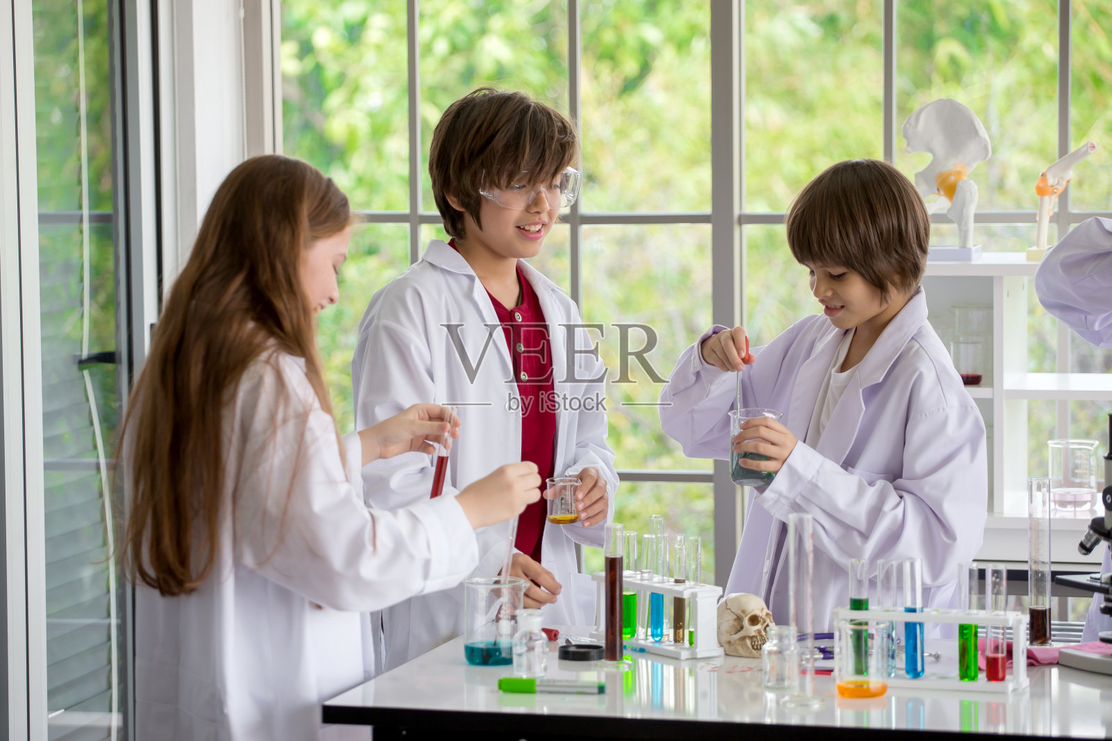 一群穿着白袍的学生在学校的实验室里做化学实验。在科学实验室里，孩子们用吸管将液体滴到试管中进行研究。、高加索、生物化学。化学课照片摄影图片