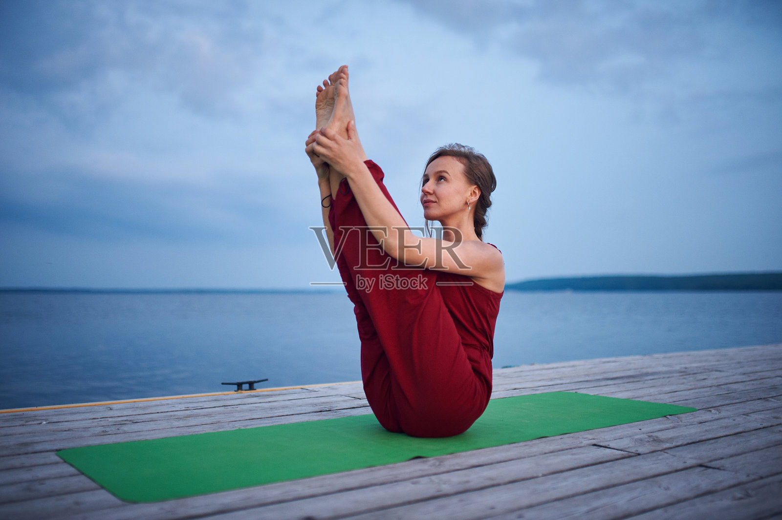 美丽的年轻女子练习瑜伽体式Paripurna Navasana在湖附近的木制甲板上照片摄影图片
