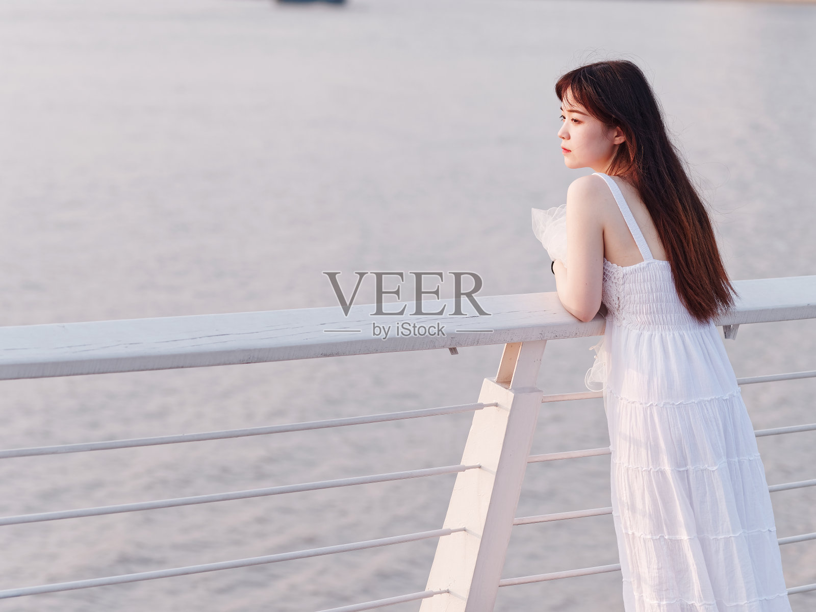 美丽的中国女孩的肖像穿着白色的新娘站在河边，看着夏天的黄昏，后视图，美丽，生活方式和夏天的概念。照片摄影图片