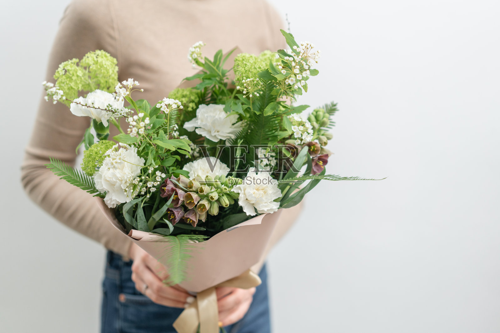 女人手里捧着两束美丽的混合鲜花。花店花匠的工作。精致柔和的颜色。新鲜切花。绿色和白色照片摄影图片