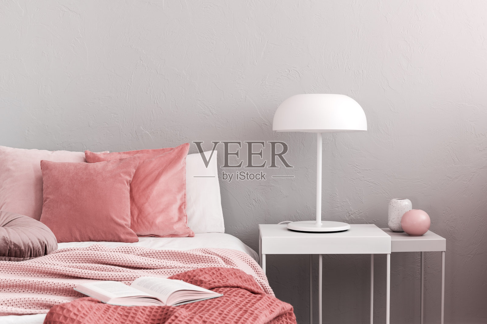 简单的床头柜上放着白色工业灯，旁边是舒适的粉红色床上用品照片摄影图片
