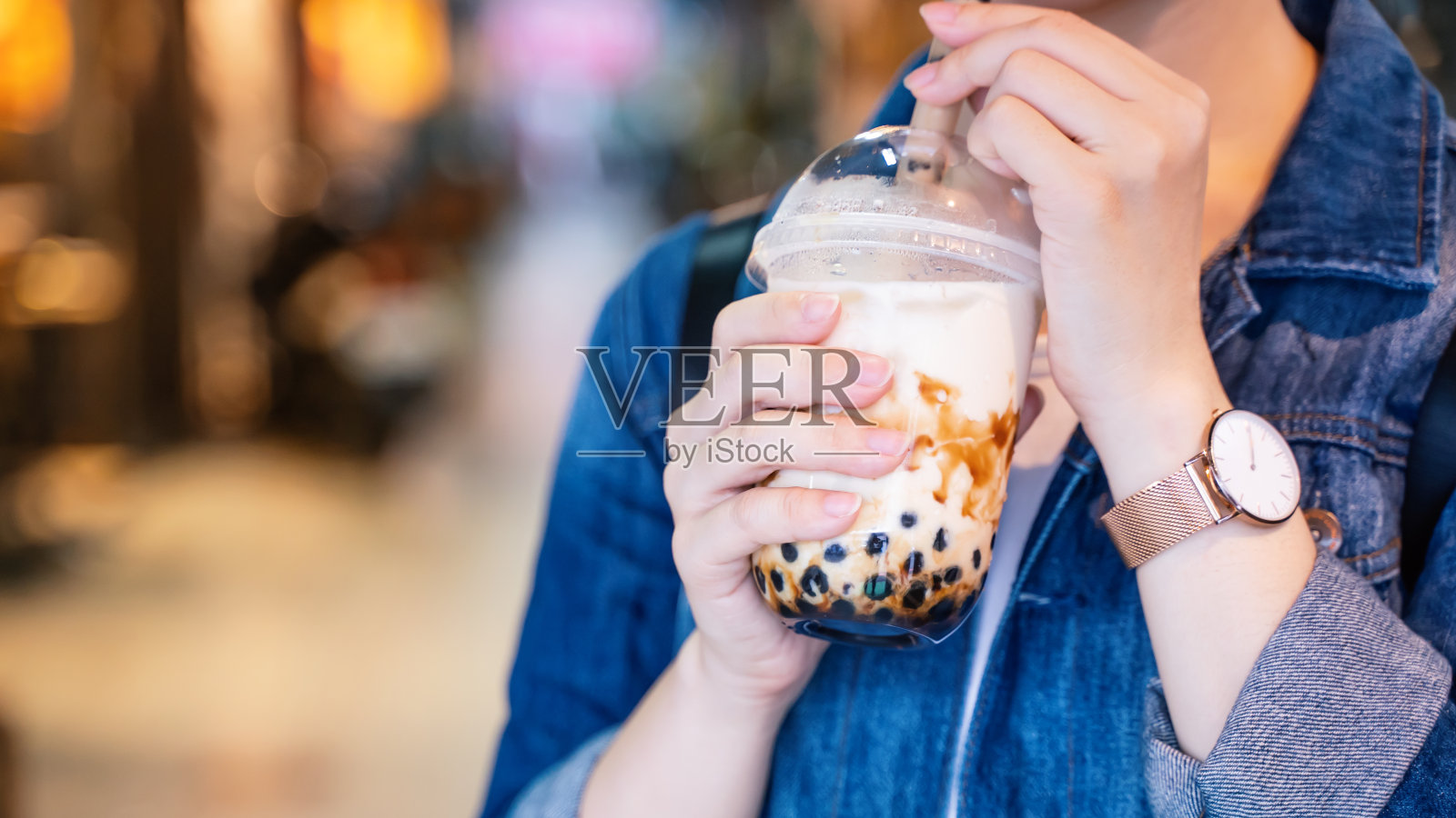 台湾夜市，一名年轻女子拿着玻璃吸管喝着红糖口味的珍珠奶茶照片摄影图片