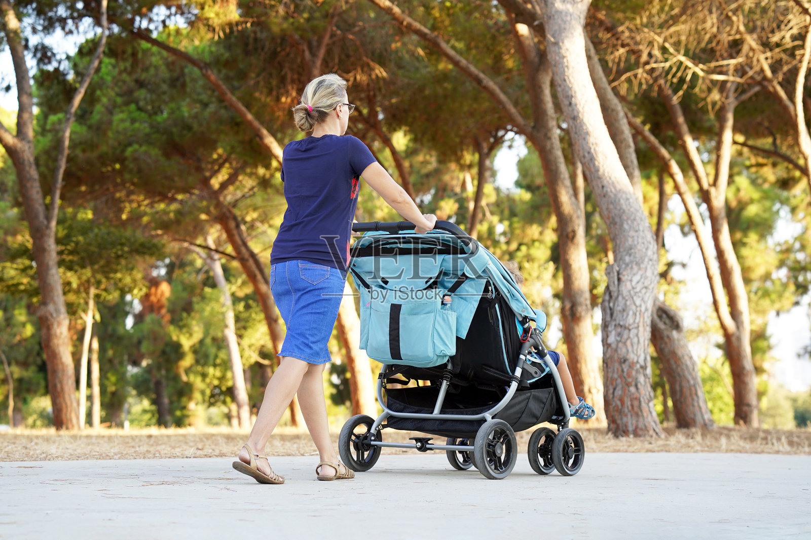 一个女人推着婴儿车在公园里散步。照片摄影图片