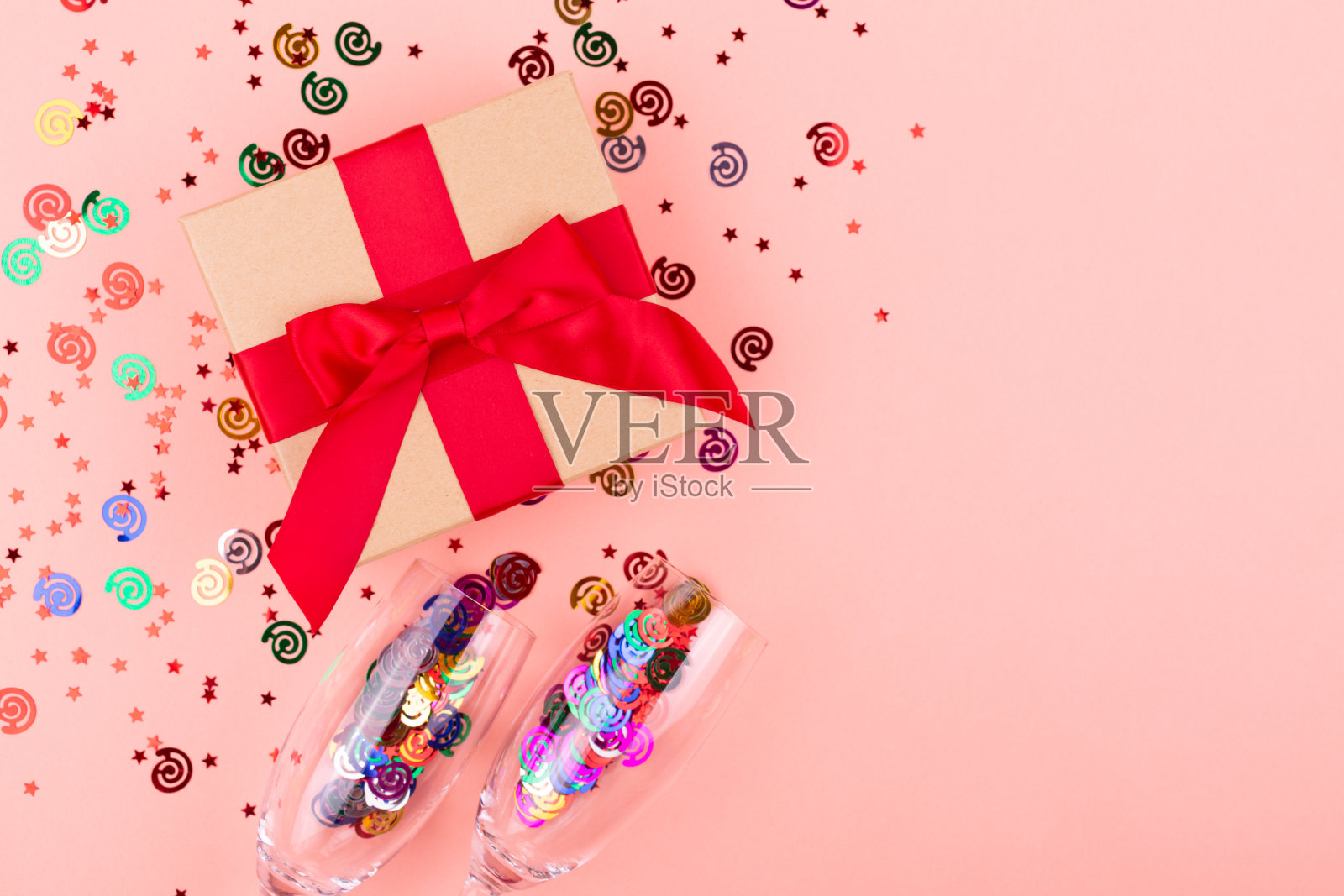 一个礼品盒，香槟酒杯，粉色背景上的五彩纸屑。照片摄影图片