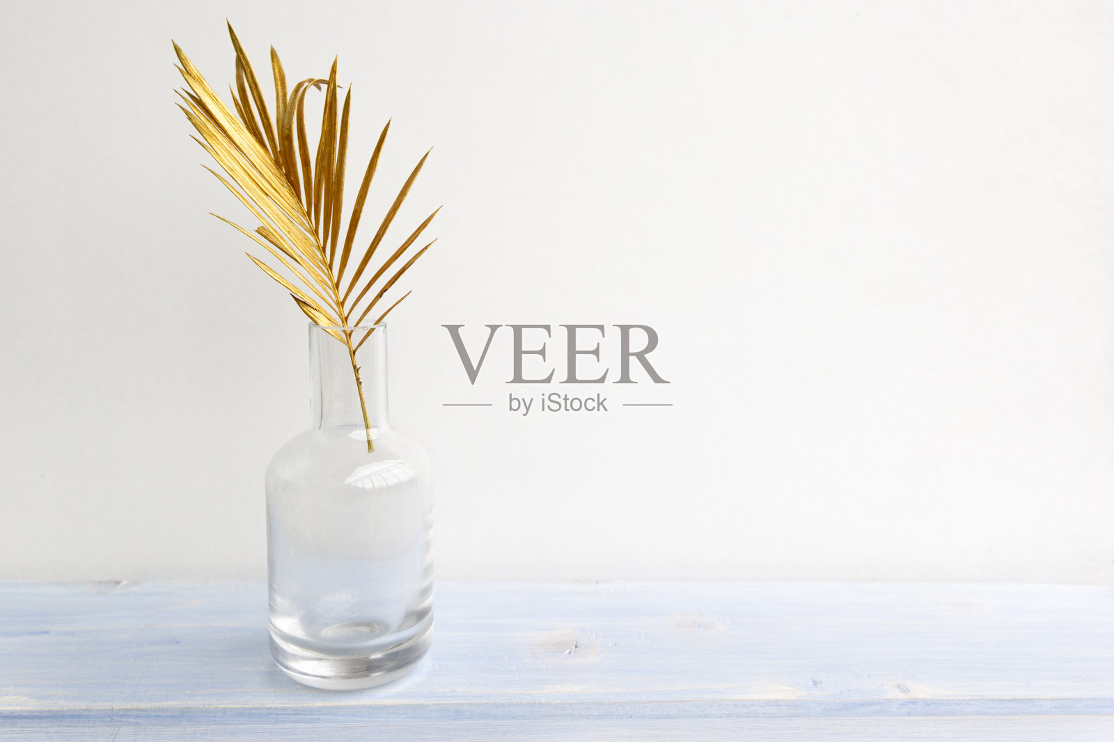 金色棕榈叶玻璃花瓶瓶在浅蓝色木制背景。创意简约现代理念的有机美趋势照片摄影图片