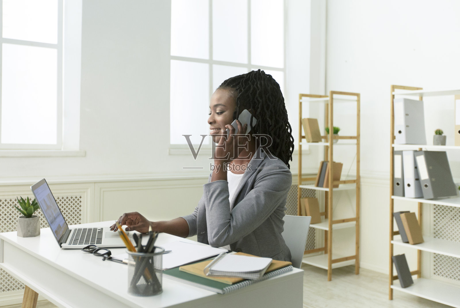 快活的黑人女士在办公室用笔记本电脑打电话照片摄影图片
