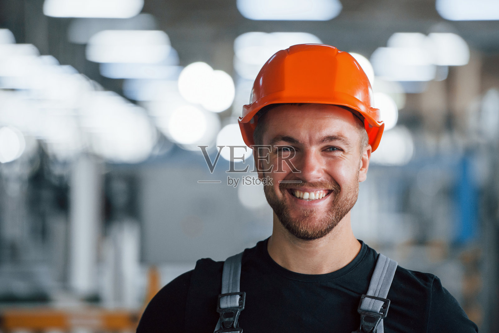 微笑和快乐的员工。工业工人在工厂室内的肖像。戴着橙色安全帽的年轻技术员照片摄影图片