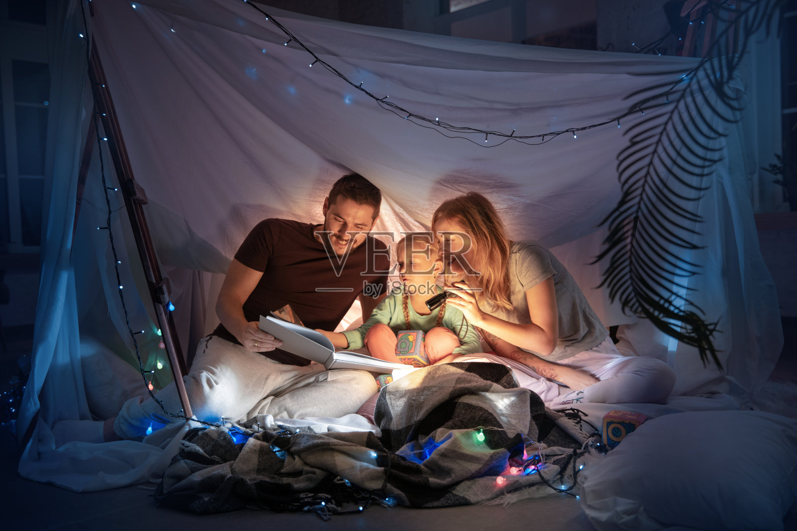 一家人坐在帐篷里，拿着手电筒读故事照片摄影图片