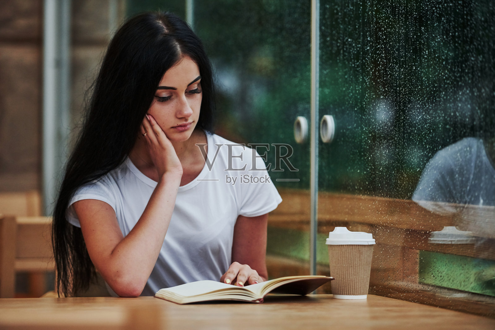 下雨天坐在咖啡馆里的年轻女学生的肖像。一个人只有照片摄影图片