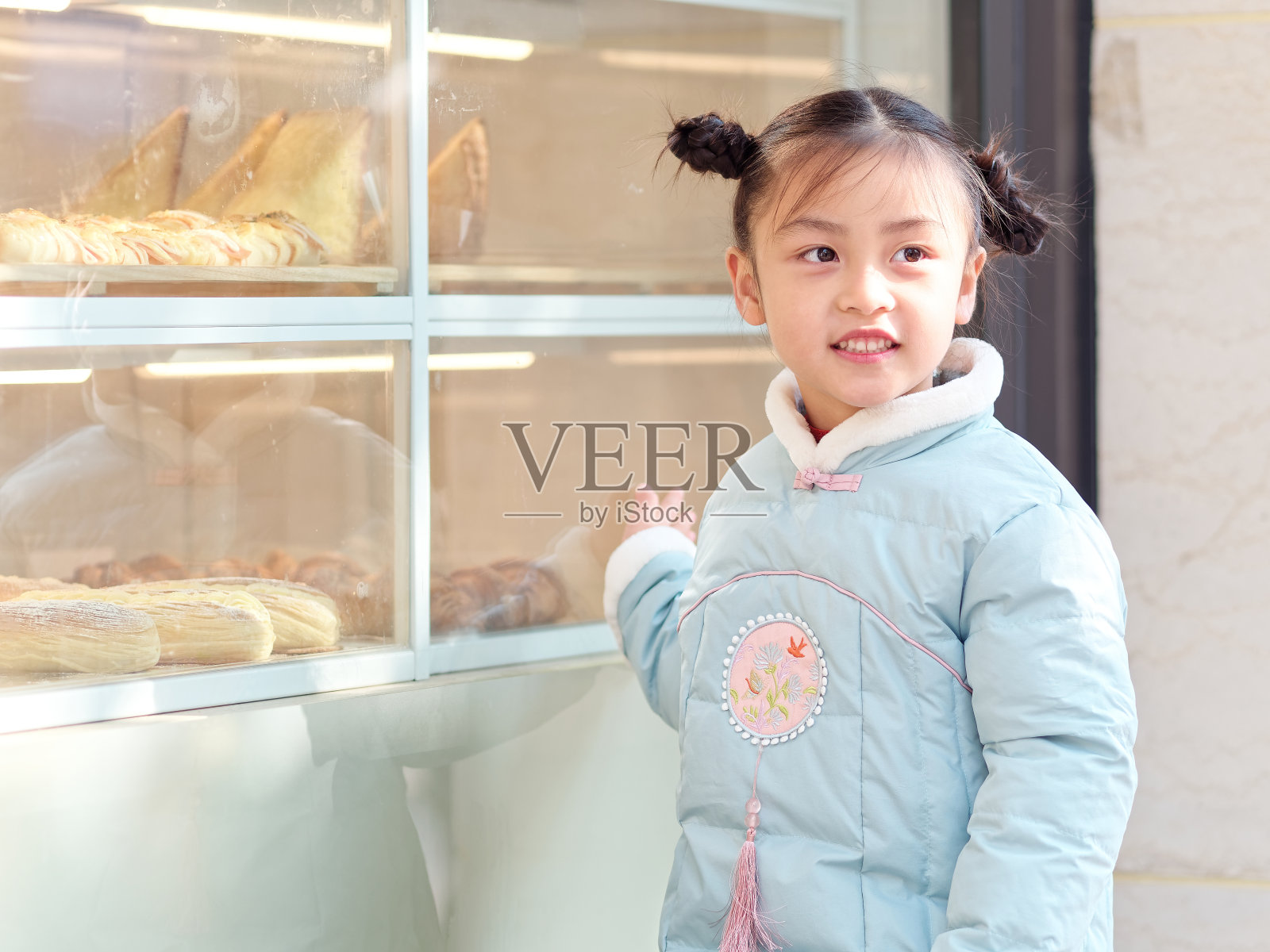 这是一个4-5岁的中国小女孩的肖像，穿着蓝色的新年衣服，看着面包店的橱窗前，传统的中国孩子的发型。照片摄影图片