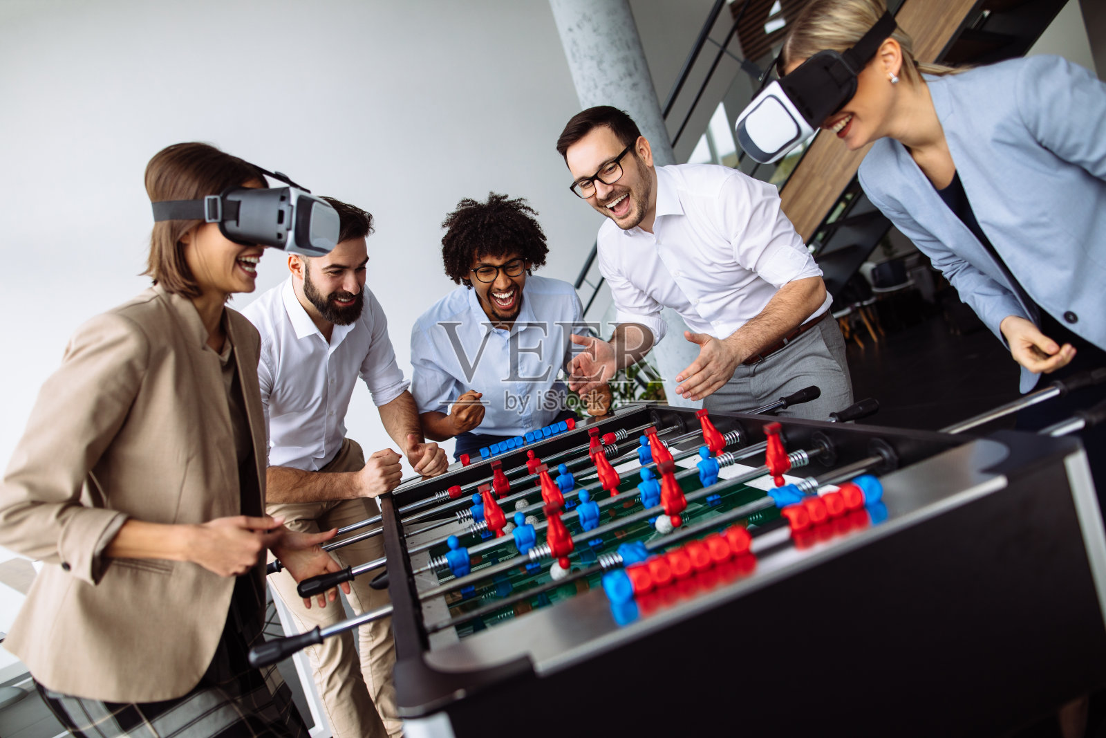 年轻的办公室职员用虚拟现实头盔玩桌上足球照片摄影图片