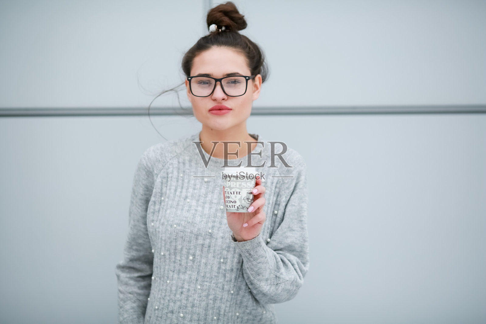 一个拿着玻璃杯靠在灰色的墙上喝咖啡的女人照片摄影图片