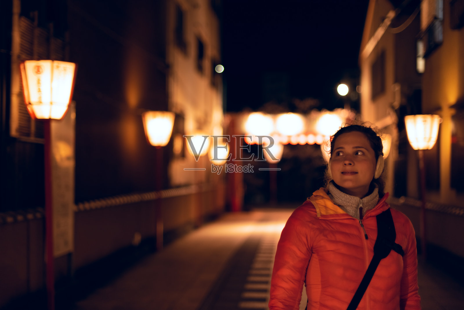 日本京都，在Gion区狭窄的小巷黑暗的街道上，年轻快乐的女人站在看着照亮的红灯笼排照片摄影图片