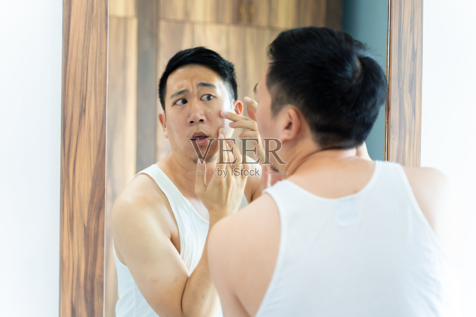困惑的亚洲男子检查痤疮问题，同时看着镜子照片摄影图片