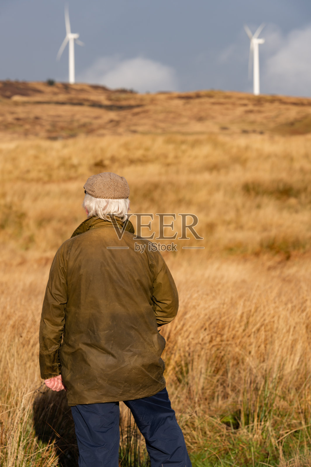 一位老人站在苏格兰西南部偏远的乡村，看着一个风力发电场照片摄影图片