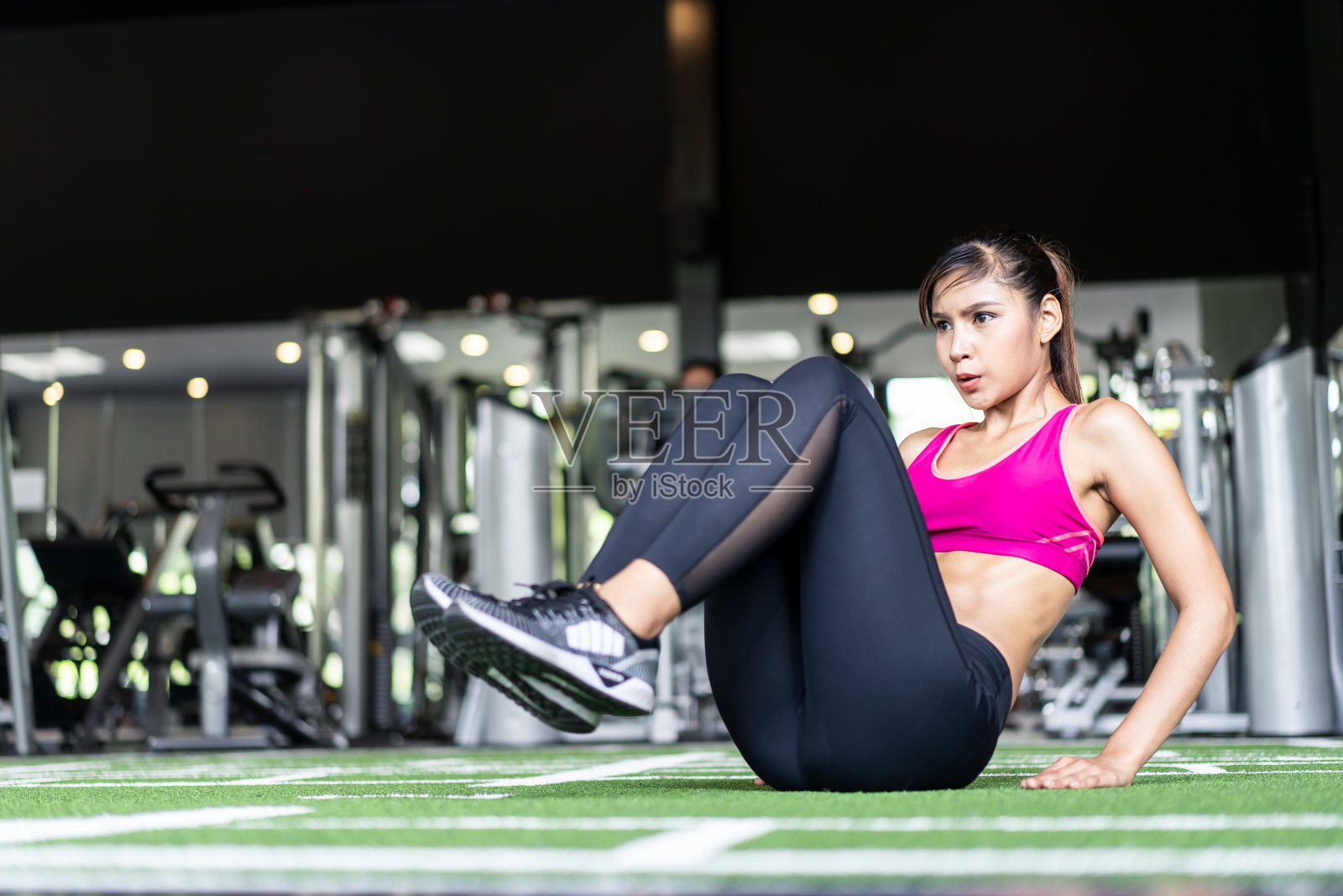 年轻健康的肌肉亚洲妇女锻炼和工作在健身房。漂亮的女孩在运动服坐在地板上，看着前面她专注于训练建立腹肌肌肉，腹部力量。照片摄影图片