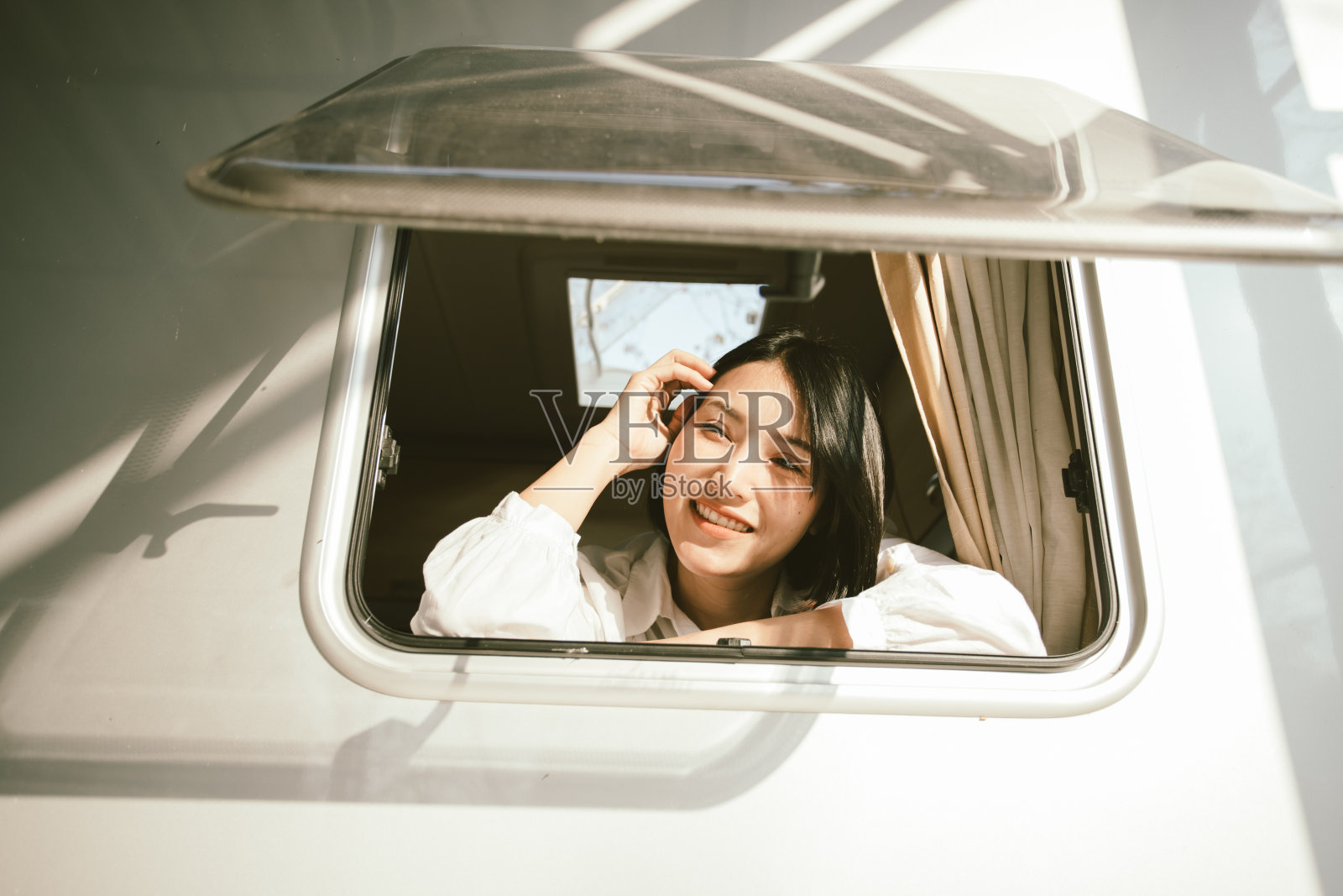 年轻的亚洲女人从露营车的窗户往外看。照片摄影图片
