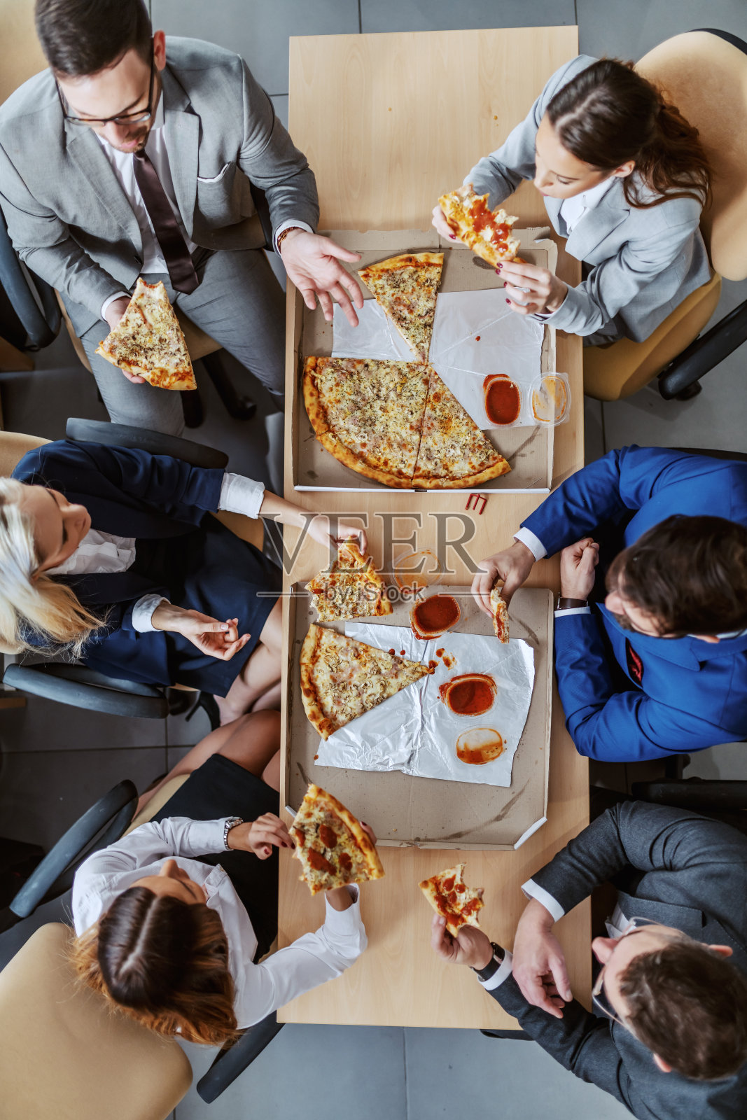 顶视图的一群商务人士坐在桌子上，吃披萨午餐和聊天。照片摄影图片