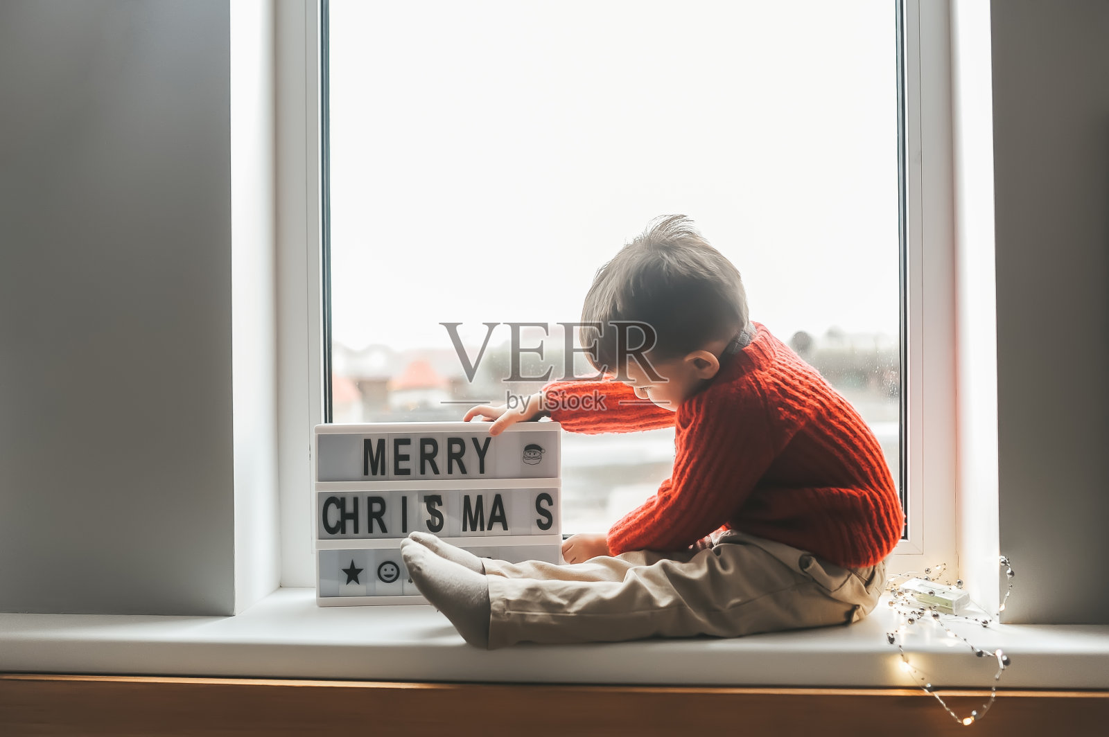 冬天的圣诞节，一个小男孩坐在窗台上照片摄影图片