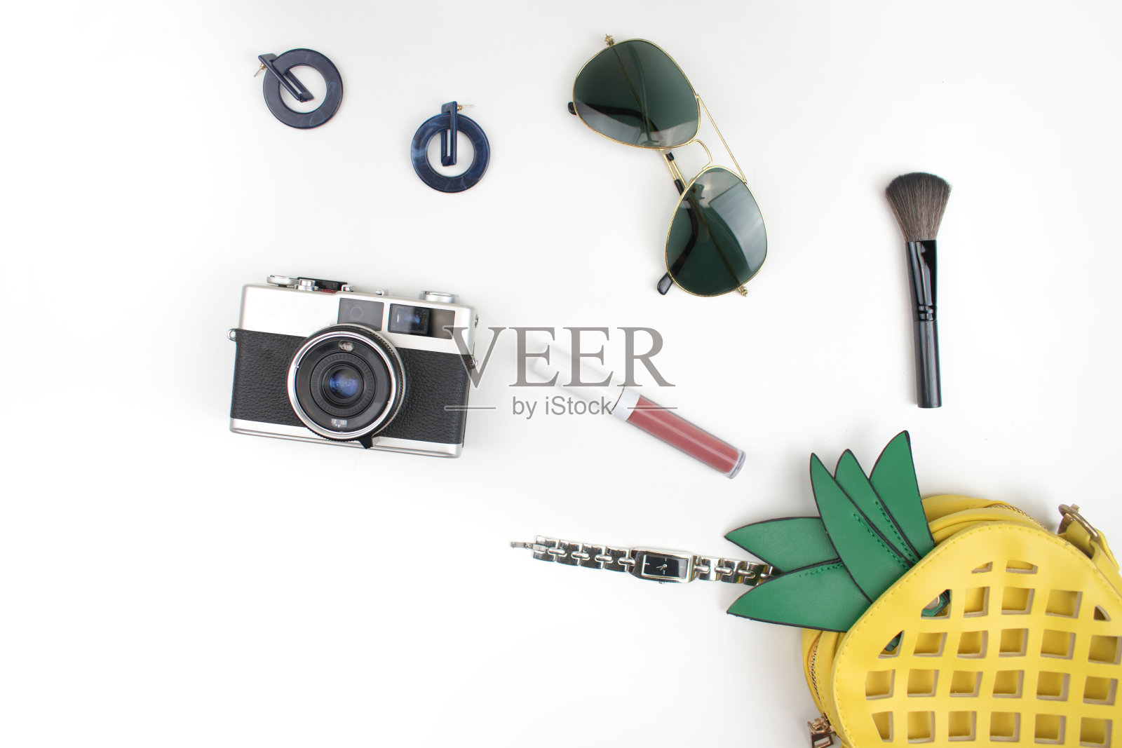 打开这个黄色的菠萝包，里面有化妆品、配饰、手表、太阳镜和以白色为背景的摄像机。平的。照片摄影图片