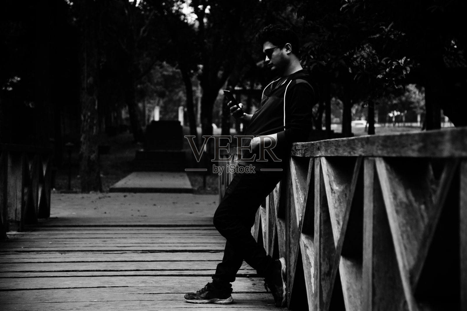 一个穿着黑衣的男人站在公园的木桥上照片摄影图片