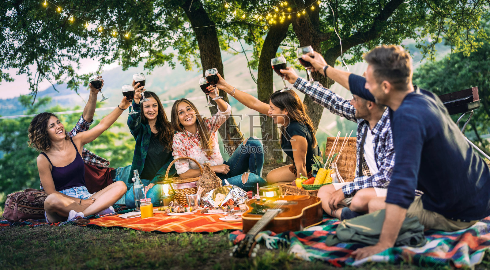 快乐的朋友有乐趣在葡萄园日落-年轻人千禧祝酒在露天野餐弦轻-青年友谊的概念与男孩和女孩喝红酒在酒吧-烧烤派对照片摄影图片