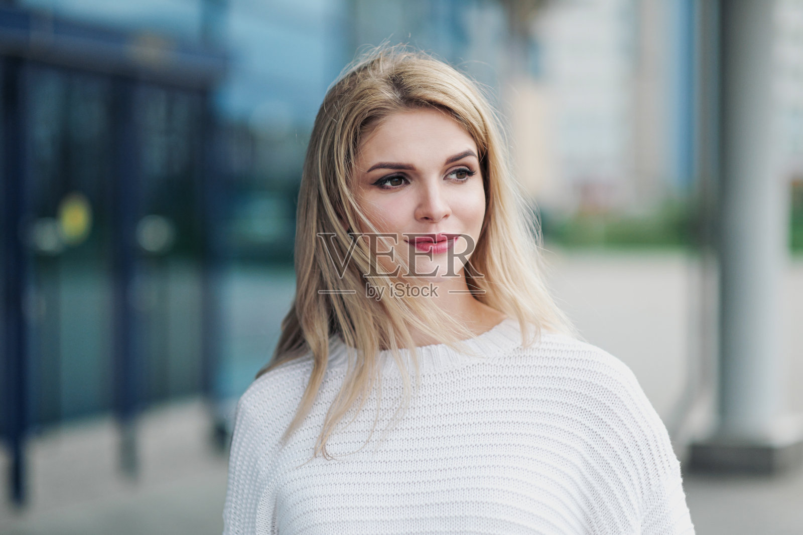 年轻迷人的金发女子肖像在白色毛衣的城市街道的背景。照片摄影图片